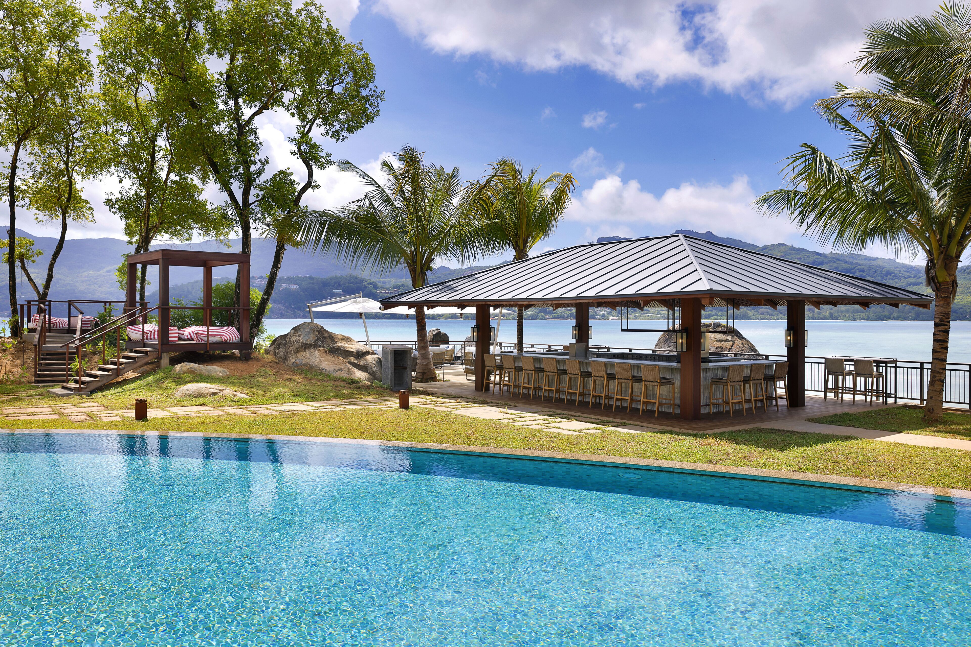A swimming pool with a covered seating area, a gazebo, and a view of the ocean and mountains.