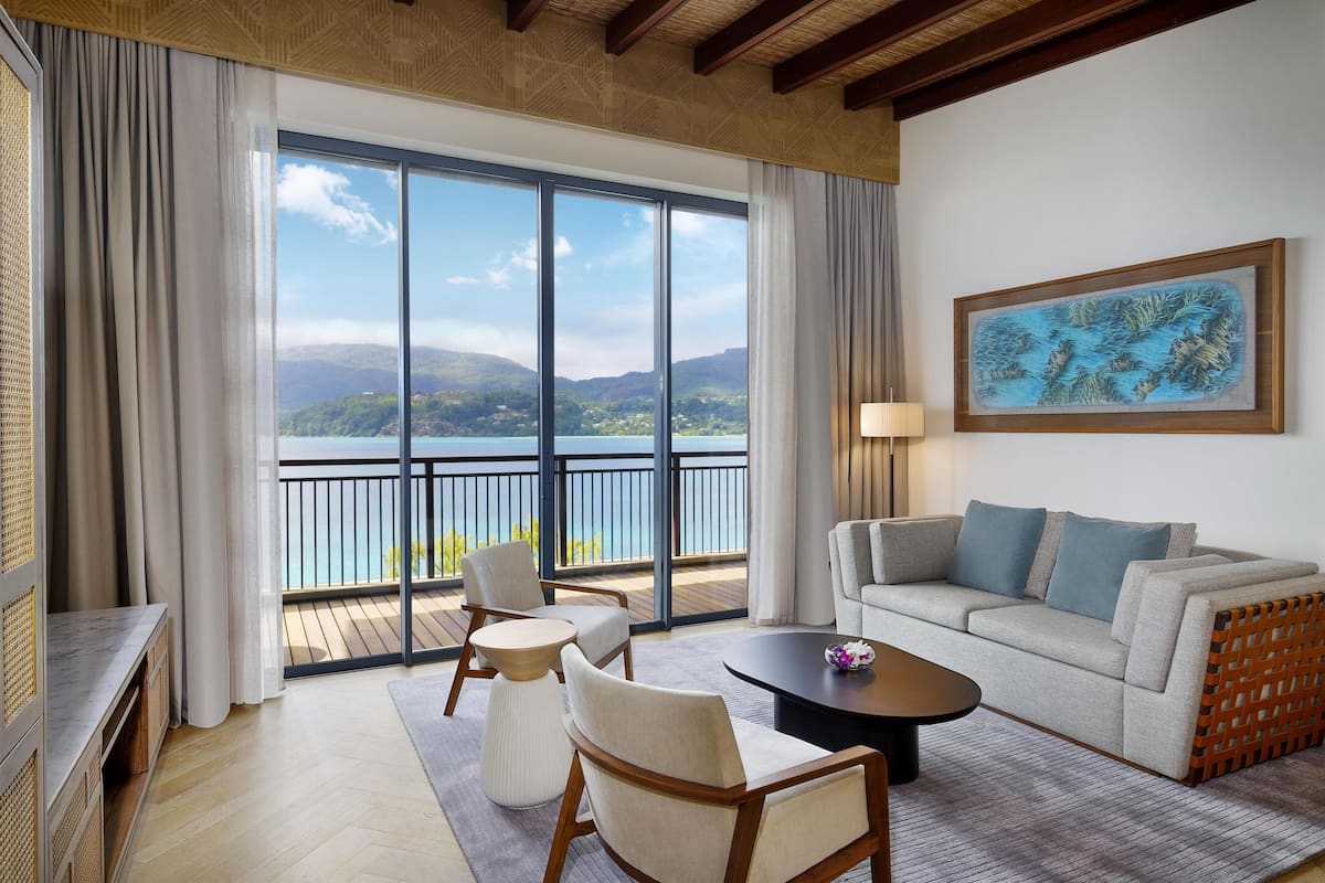 A room with a balcony, a sofa, chairs, a coffee table, and a painting.