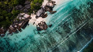 Ein Luftbild von einem Strand mit klarem, türkisblauem Wasser, Felsformationen und dichter, grüner Vegetation.