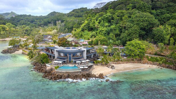 Ein Resort mit mehreren Gebäuden, einem Strand und einem klaren türkisblauen Meer.