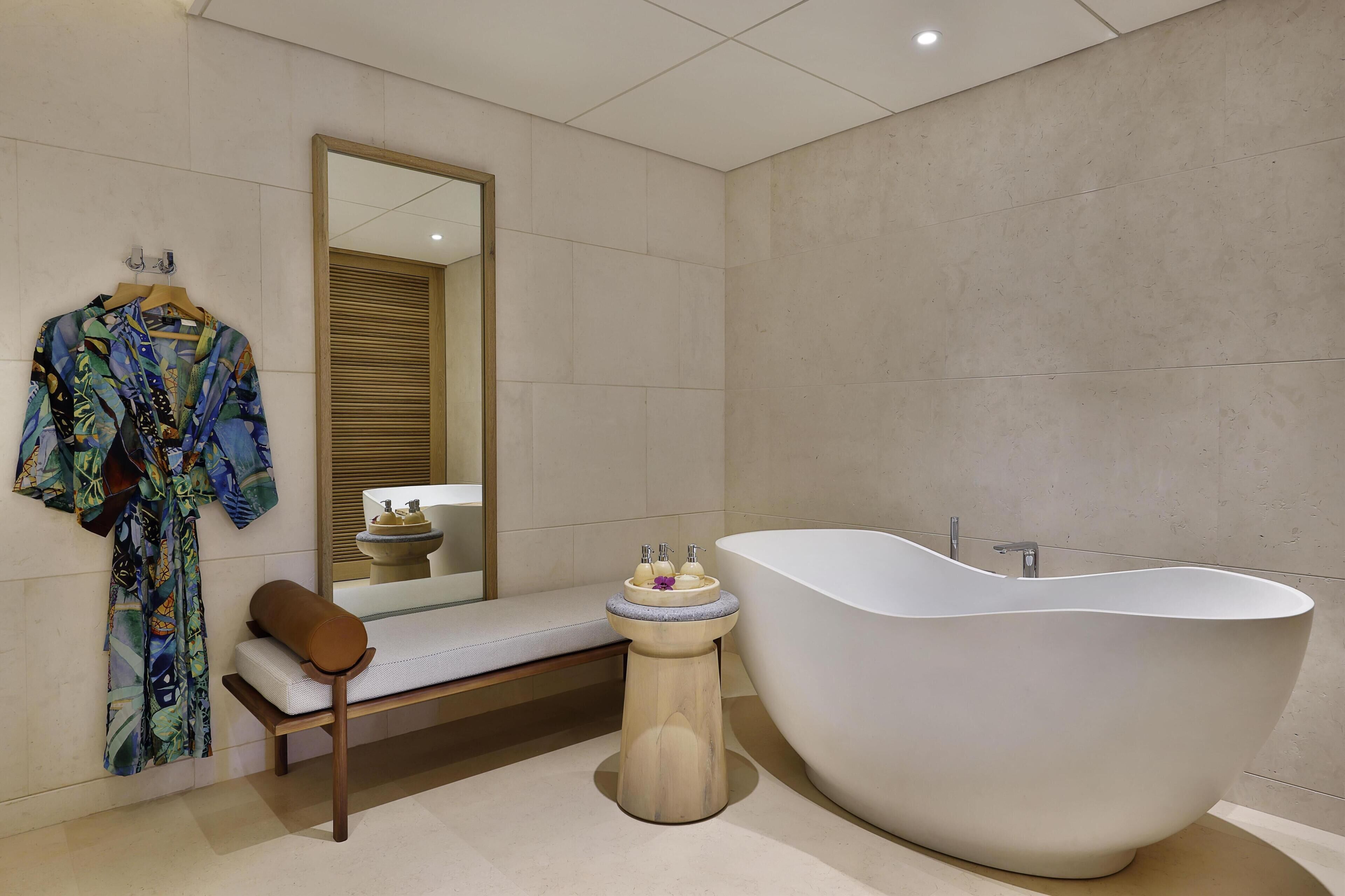 Ein modernes Badezimmer mit einer freistehenden Badewanne, einer Sitzbank und einem Bademantel, der an der Wand hängt.