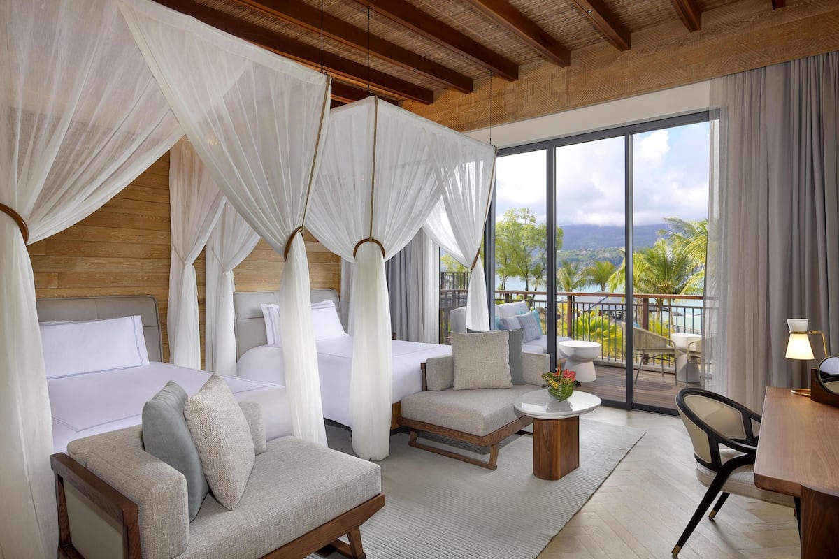 A hotel room with a bed, a sofa, a small table, and a balcony with a view.
