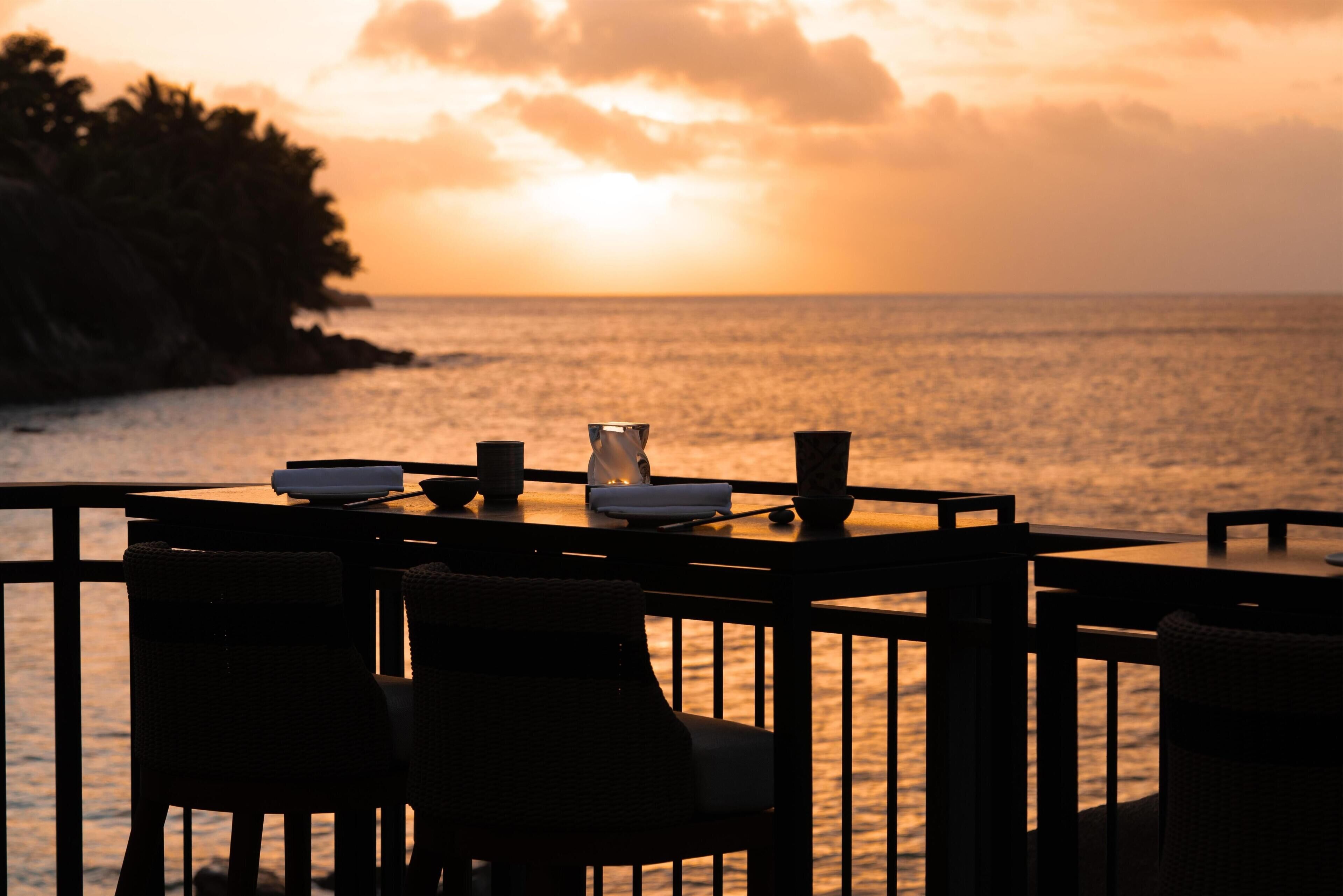 Mesa para dos con sillas, con vista a un cuerpo de agua al atardecer.