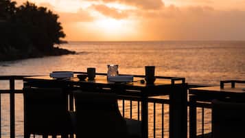 Mesa para dos con sillas, con vista a un cuerpo de agua al atardecer.