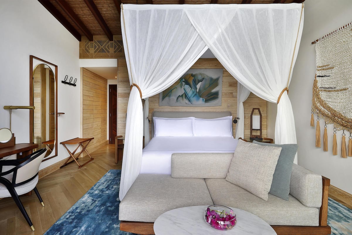 A bedroom with a bed, a sofa, a small table, a chair, and a mirror.