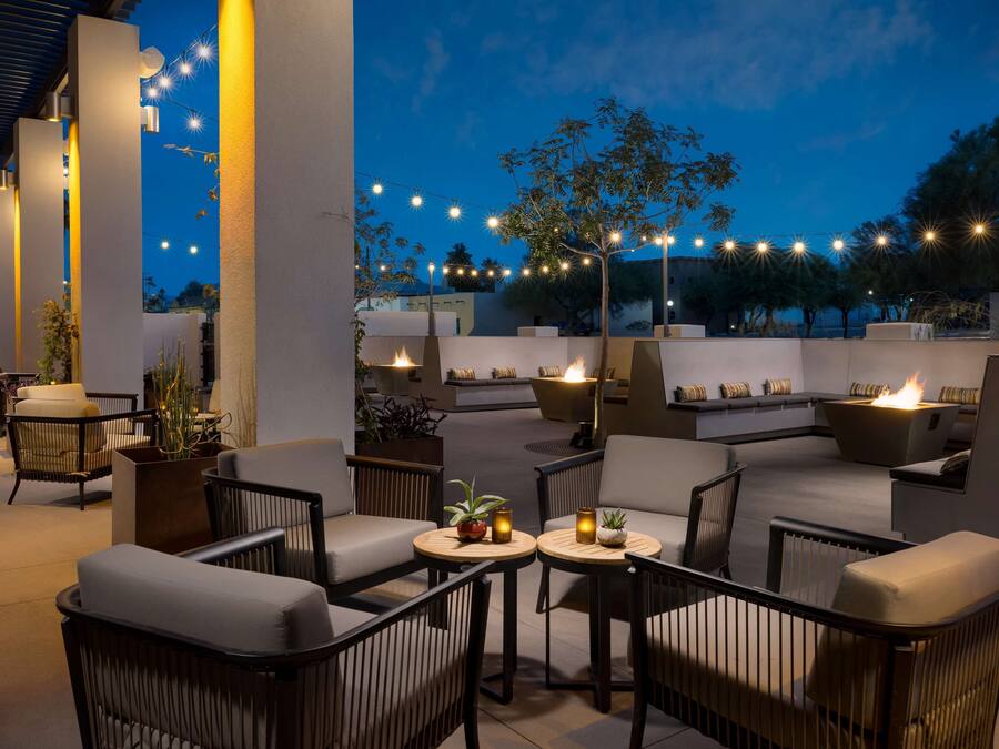 An outdoor seating area with sofas and tables, string lights, and a fire feature.