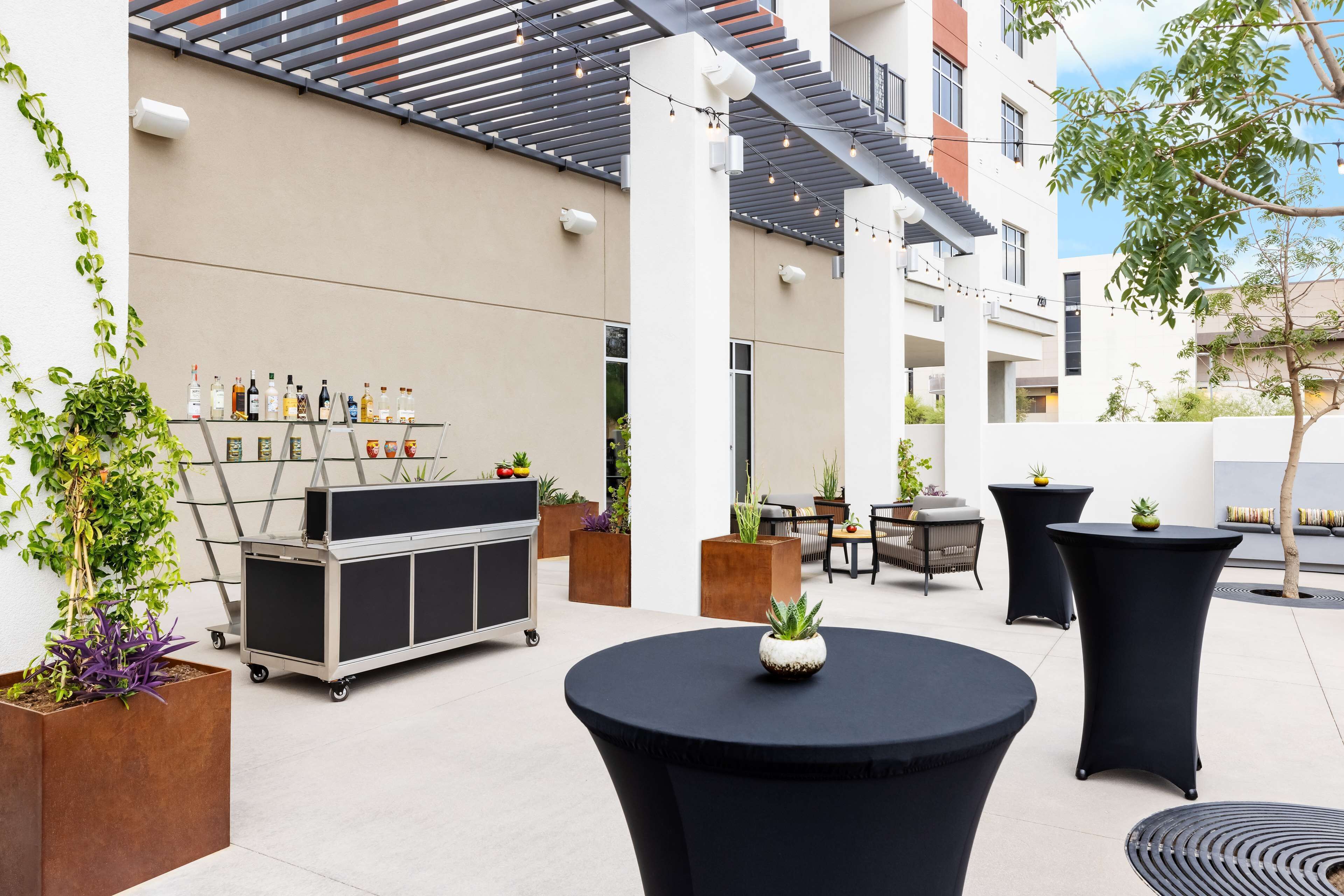 An outdoor patio area with round tables, potted plants, and a beverage cart.