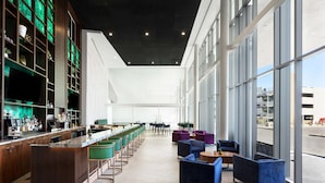 A modern bar area with a long counter, multiple stools, and a seating area with sofas and tables. - DoubleTree by Hilton Tucson Downtown Convention Center (Tucson)