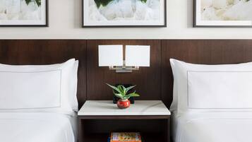 Habitación de hotel con dos camas, una mesita de noche con planta en maceta, un libro y cuadros en la pared.