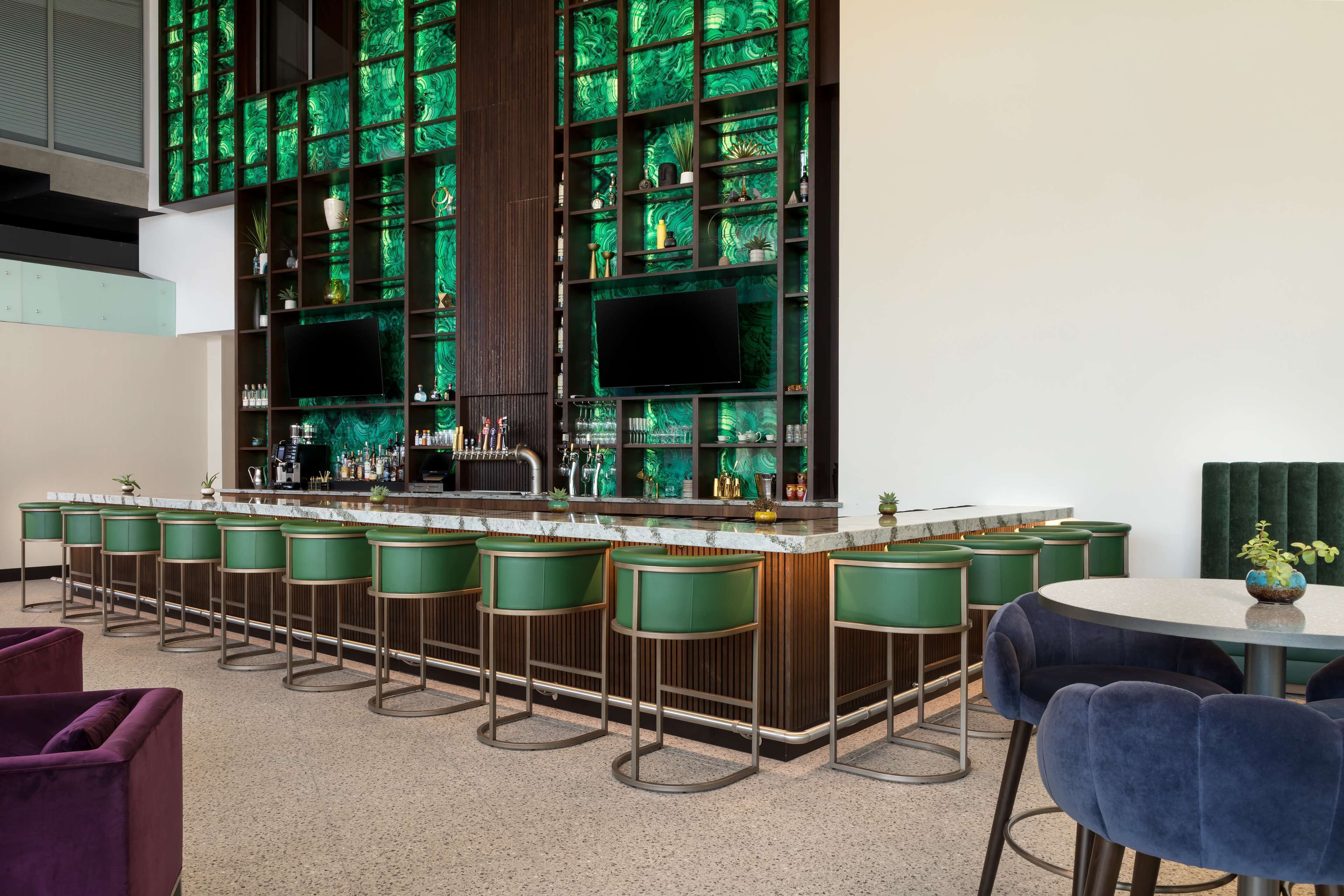 Uma área de bar com banquetas verdes, uma mesa redonda e uma TV fixada na parede.