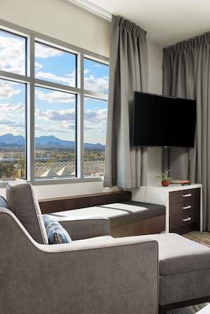 A modern living room with a large window, a flat-screen TV, a sofa, and a small side table with a plant.