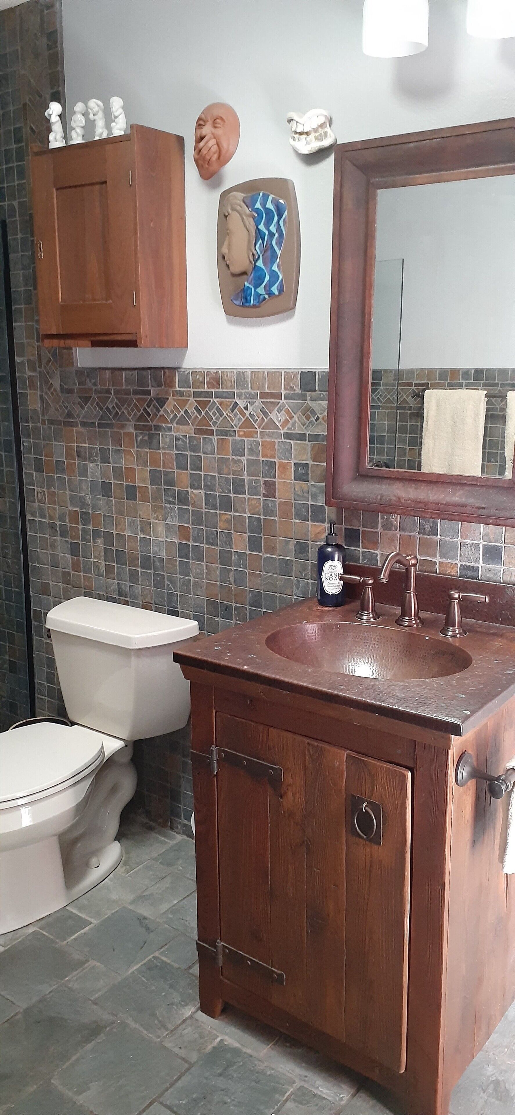 A bathroom with a wooden vanity, a large mirror, a tiled backsplash, and a toilet.