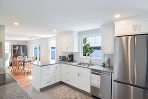 A modern kitchen with white cabinets, a stainless steel refrigerator, and a view of the sea through the window. - Waterfront on the Cove, NEW Kitchen and Central AC (Orleans)
