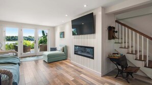 A spacious living room with a large TV, a comfortable sofa, a dining area with a wooden table, and a staircase. - Waterfront on the Cove, NEW Kitchen and Central AC (Orleans)