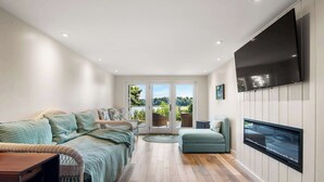 A modern living room with a sofa, armchair, and a TV mounted on the wall. - Waterfront on the Cove, NEW Kitchen and Central AC (Orleans)