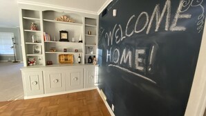 A room with a white cabinet containing various items, a blackboard with 'WELCOME HOME!' written on it, and a wooden floor. - 12th Green at Duncan Golf Club and Tennis Club (Duncan)