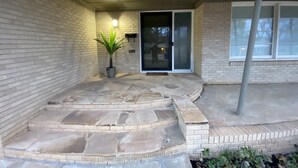 A covered outdoor area with a brick wall, a potted plant, a set of stone steps, and a sliding glass door. - 12th Green at Duncan Golf Club and Tennis Club (Duncan)