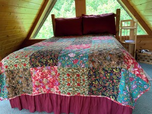 Ein Schlafzimmer mit einem großen Bett, einem Holzkopfstück und einem Fenster mit Blick auf Bäume.