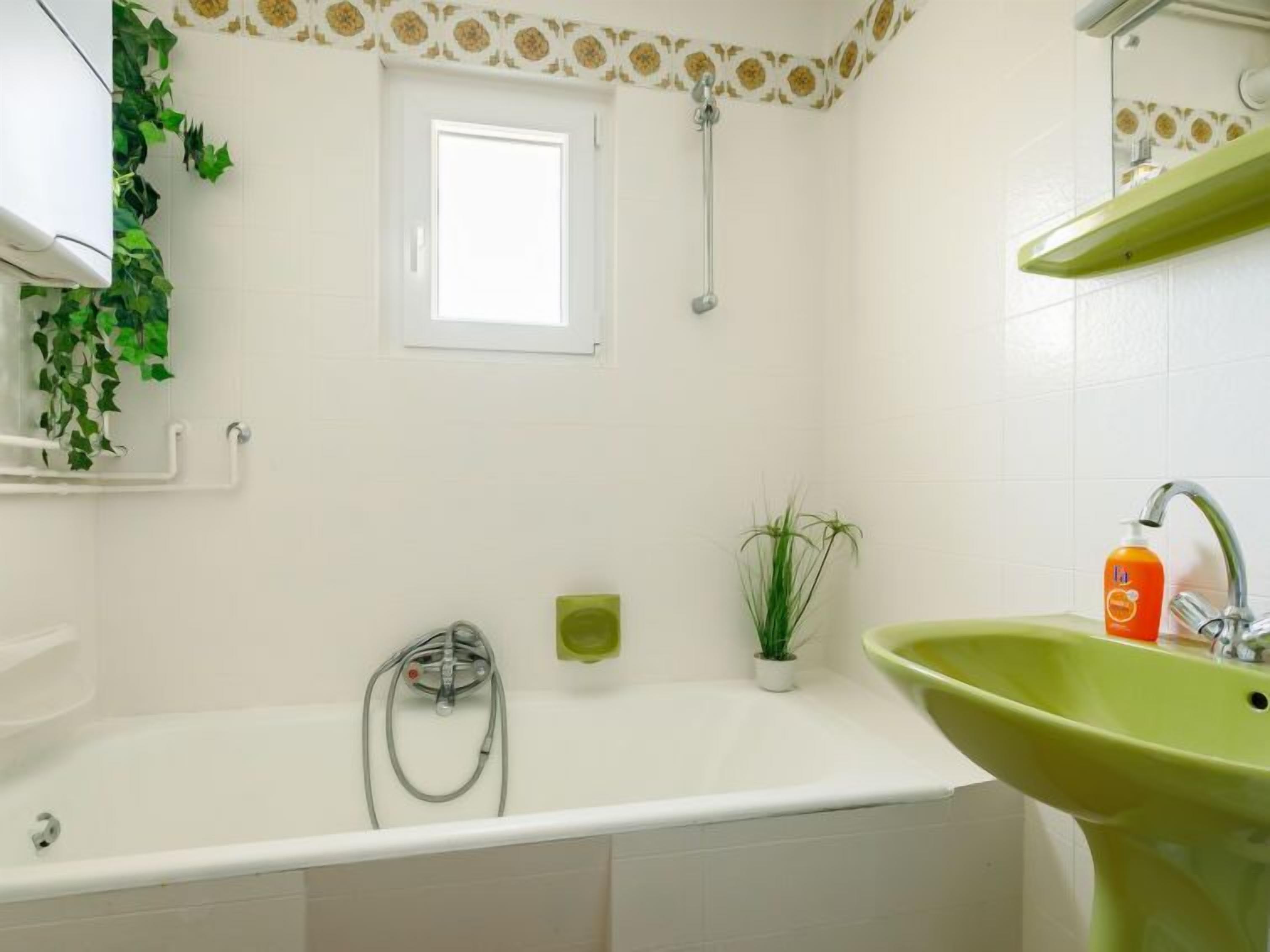 Un baño con bañera, un lavabo verde, una ventana y una ducha.