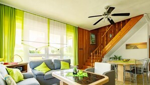 A living room with a sofa, a coffee table, a dining table with chairs, a staircase, and a ceiling fan. - Sunny Day by Interhome (Balatonmariafurdo)