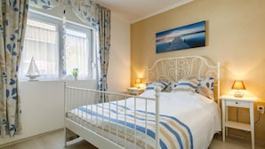 A bedroom with a bed, two bedside tables, a window with curtains, a painting on the wall, and a small sailboat decoration. - Sunny Day by Interhome (Balatonmariafurdo)