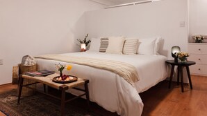 A bedroom with a large bed, bedside tables, a bedside lamp, a small table with a tray of fruit and a book, and a decorative vase with flowers.