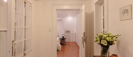 A hallway with a wooden bench, a vase with flowers, and a framed picture on the wall.