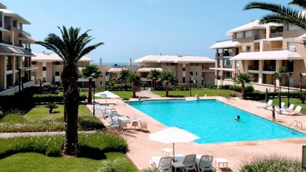 Een resort met een zwembad, omringd door palmbomen en ligbedden.