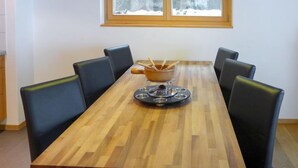 Un tavolo da pranzo in legno rettangolare con sei sedie nere, una ciotola per cani al centro e una finestra che si affaccia su un paesaggio innevato.