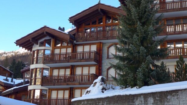 Un edificio in legno a più piani con balconi, circondato da neve e alberi.