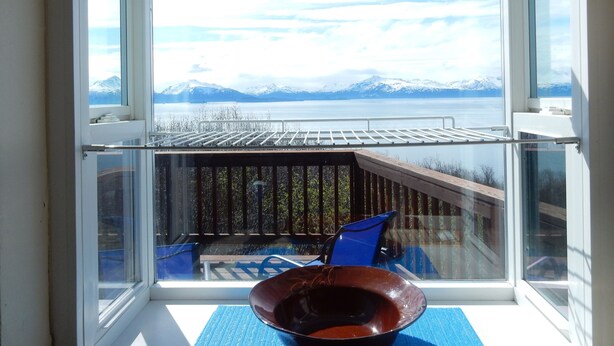 A room with a large window overlooking a lake and mountains. - Upper Moose Caboose (Homer)