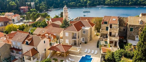 A coastal residential area with stone buildings, a swimming pool, and a view of the sea with boats.