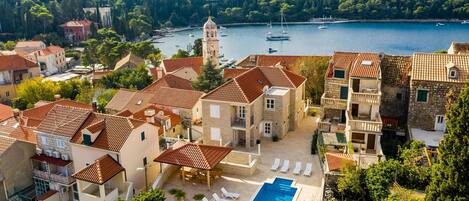 A coastal residential area with stone buildings, a swimming pool, and a view of the sea with boats.