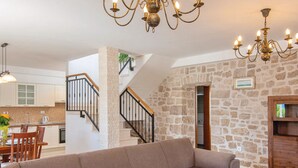 Un salón espacioso con un amplio sofá beige tipo seccional, una mesa de centro de madera y una pared de piedra. Una escalera con barandilla negra conduce a un nivel superior.
