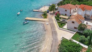 Una zona costera con barcos amarrados en un muelle, una playa de arena y edificios residenciales con tejados de teja roja.
