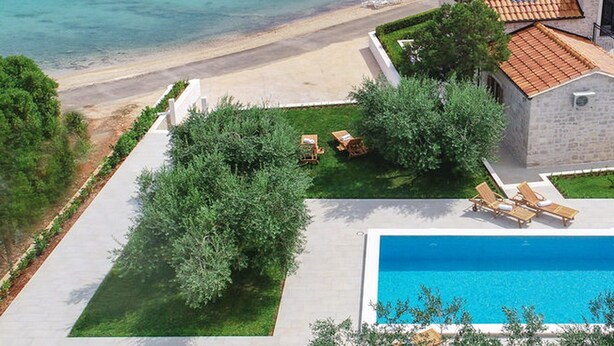 Una villa costera con piscina, muelle y barcos al fondo.
