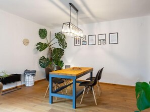 Ein Essbereich mit einem Holztisch, blauen Stühlen, einer Hängeleuchte und gerahmten Bildern an der Wand.