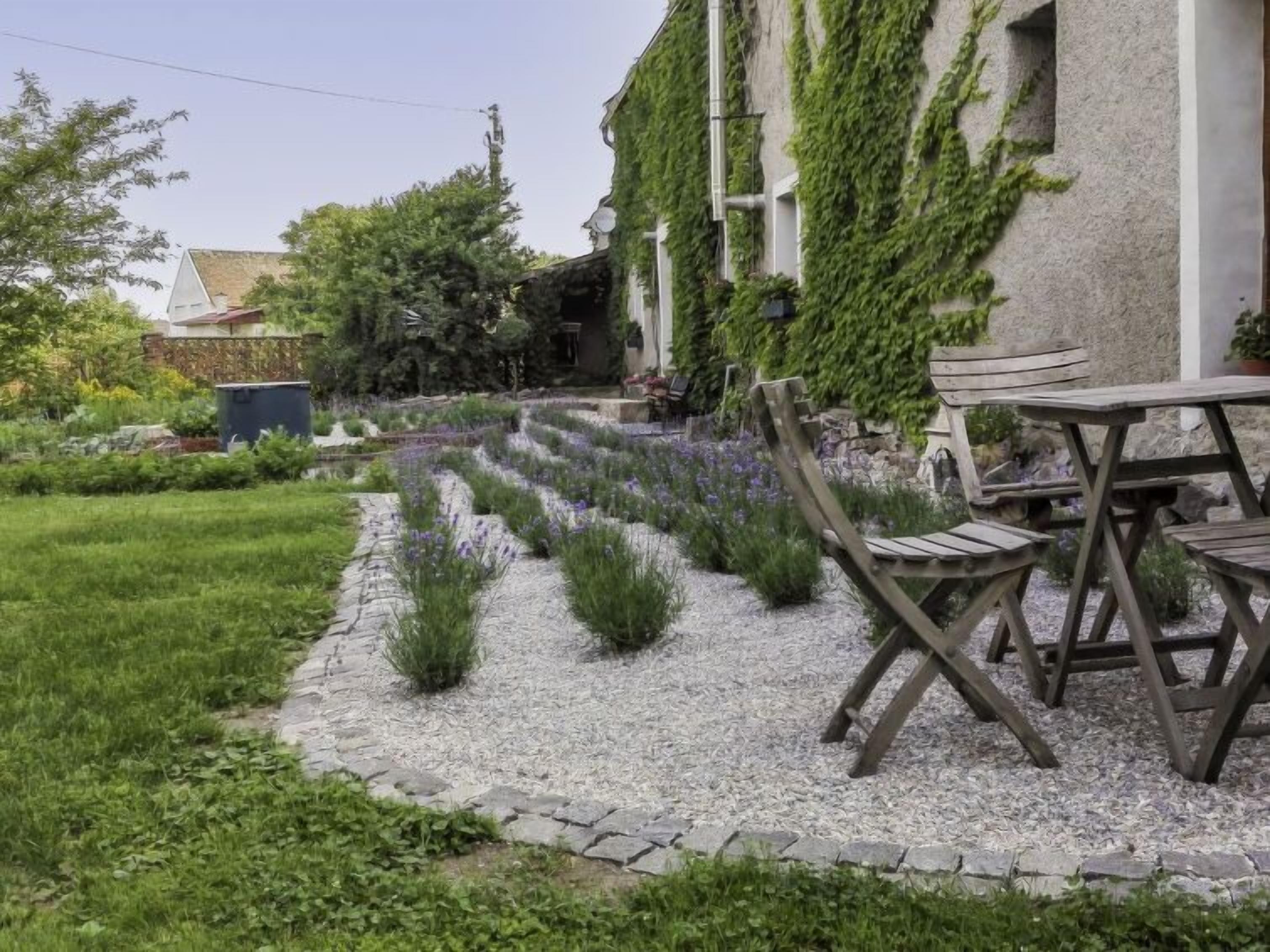 Un jardin avec un chemin de gravier, des chaises en bois et un bâtiment recouvert de lierre.