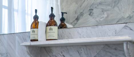 A bathroom with a marble sink, two faucets, and a shelf holding three bottles.