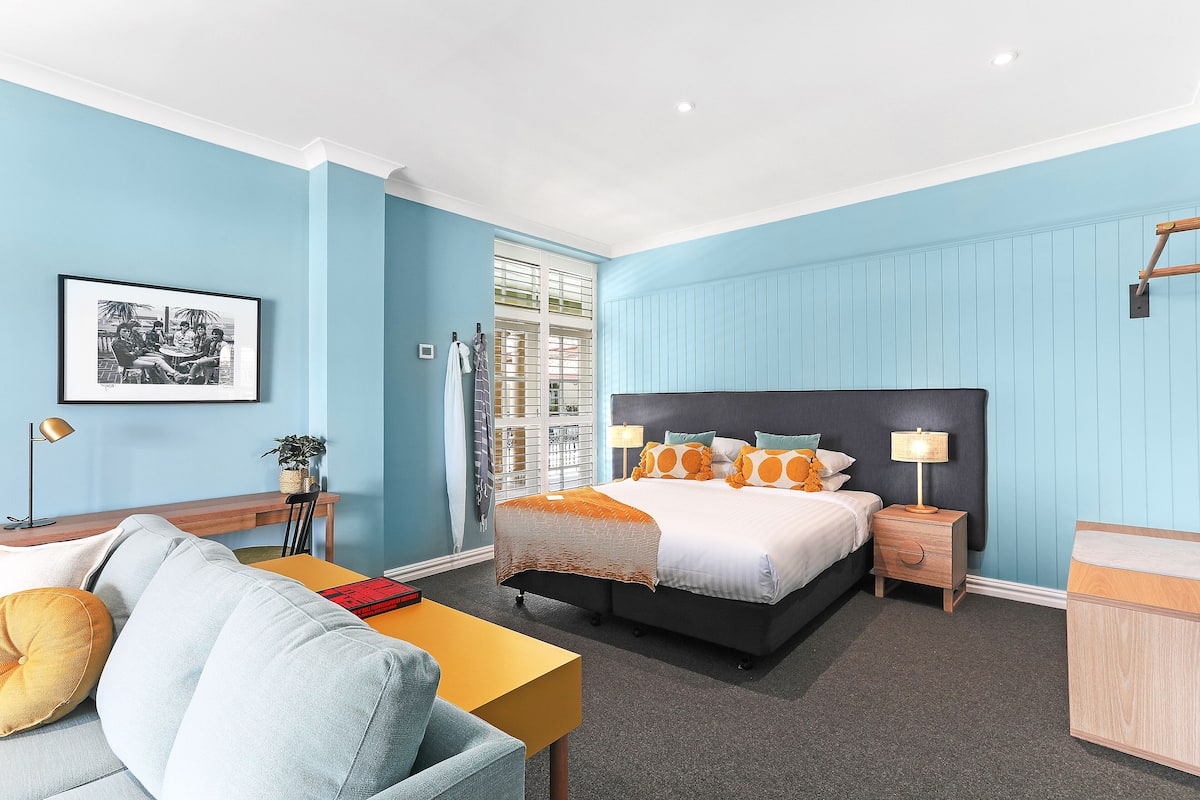 Une chambre à coucher comprenant un lit, des tables de chevet, un bureau, une chaise et un tableau encadré accroché au mur.