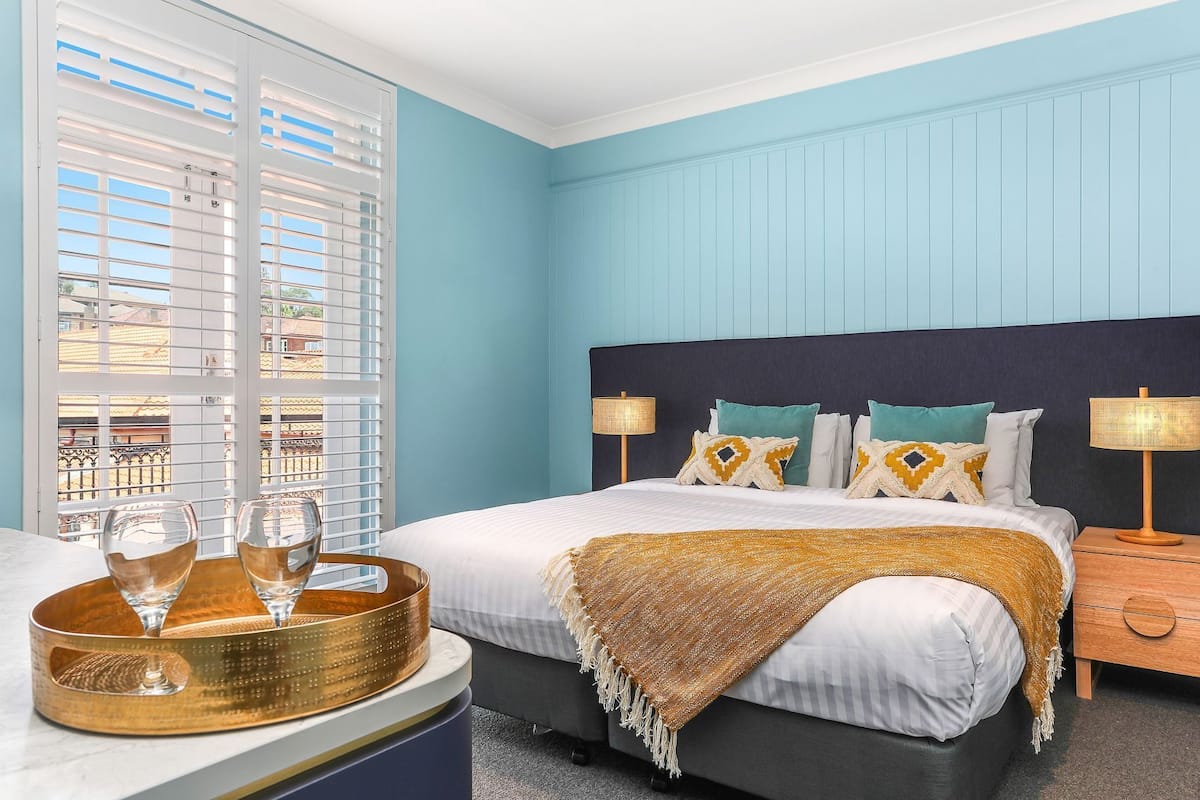 Une chambre d’hôtel avec un lit, des lampes de chevet, un plateau avec des verres et une vue par la fenêtre.