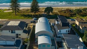 A coastal residential area with houses, a large cylindrical building, and a beach in the background. - Modern Marine Parade Apartment (Bay of Plenty)