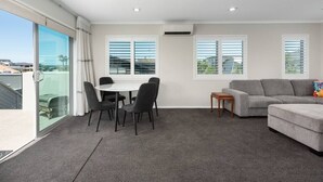 A spacious living area with a dining table and chairs, a grey sofa, and a small side table. - Modern Marine Parade Apartment (Bay of Plenty)