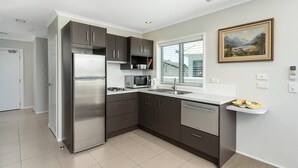 A modern kitchen with dark cabinets, stainless steel appliances, and a window with blinds. - Modern Marine Parade Apartment (Bay of Plenty)