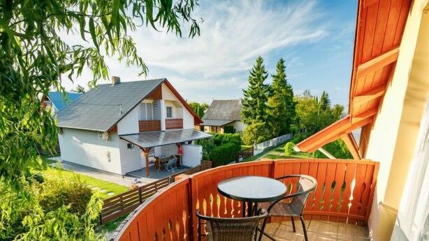 Ein Balkon mit Tisch und Stühlen mit Blick auf ein Haus und viel Grün.