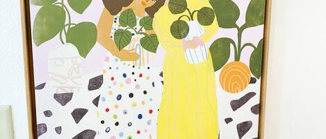 Une œuvre d’art encadrée représentant deux femmes entourées de plantes, le tout sur fond de mur blanc.