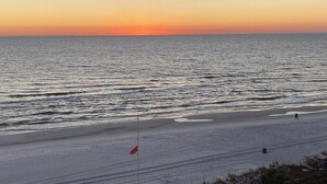 A beach with a flag, a person walking, and a sunset. - 4th floor beachfront studio with two queens (Panama City Beach)