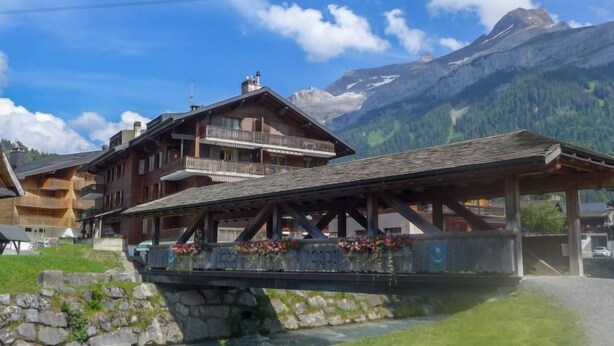 Un chalet en bois doté de balcons donnant sur une rivière, situé dans un cadre montagneux.