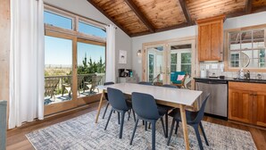 A dining area with a large table and chairs, wooden ceiling beams, and a view of the outdoors. - Bayfront on Broadkill Beach! 1810 S Bayshore (Milton)