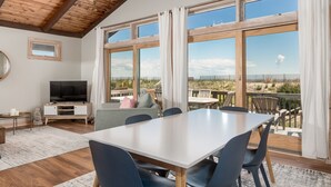 Ein großzügiger Wohnbereich mit einem großen Tisch und Stühlen, einem Fernseher und einem Balkon mit Landschaftsblick.